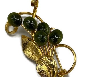 May include: A gold-toned brooch with a floral design featuring green glass beads. The brooch has a delicate, intricate design with leaves and stems.