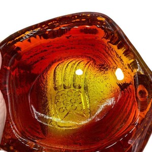 May include: A vintage orange and yellow glass ashtray with a raised design of a hand. The ashtray is made of thick glass and has a slightly irregular shape.
