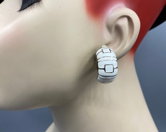 May include: White hoop earrings with a geometric design in gold. The earrings are made of ceramic and have a glossy finish.