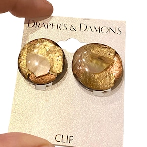 May include: A pair of gold and brown clip-on earrings with a shell-like design. The earrings are on a white card with the text "Drapers & Damons's" and "CLIP".