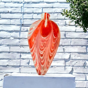 May include: A red and white glass vase with a swirling pattern. The vase is shaped like a heart and has a narrow neck.