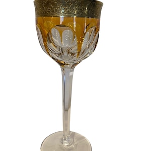 Puede incluir: Un vaso alto y transparente con un borde dorado y una base de color ámbar. El vaso tiene un diseño de cristal tallado y un tallo largo y delgado.