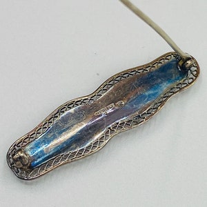 May include: A silver filigree brooch with a pin on the back. The brooch is marked "STERLING" on the back.