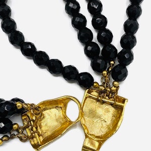 Pu&ograve; includere: Una collana di perle nere con una chiusura dorata. La collana &egrave; realizzata con perle sfaccettate e ha una chiusura unica e decorata.