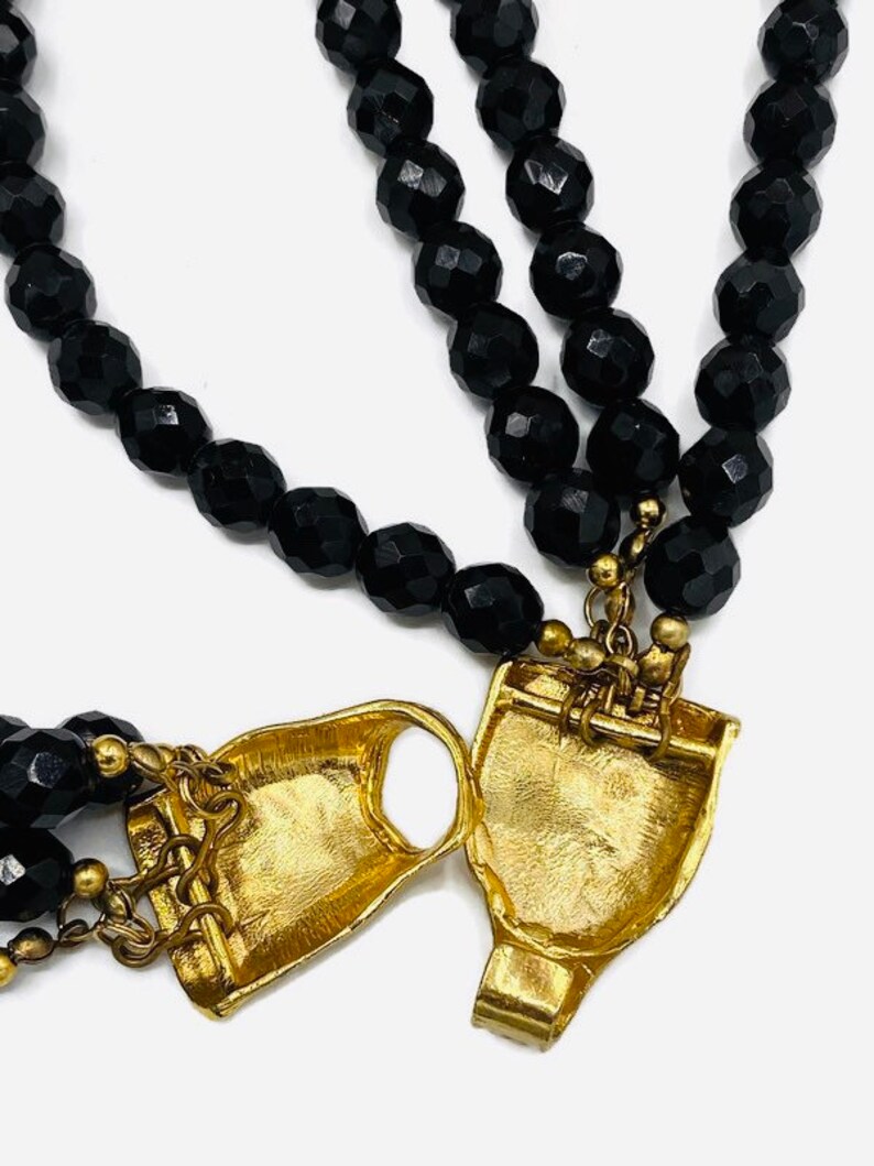 Pu&ograve; includere: Una collana di perle nere con una chiusura dorata. La collana &egrave; realizzata con perle sfaccettate e ha una chiusura unica e decorata.