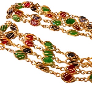 May include: A multi-strand gold chain necklace with green, red, and purple oval-shaped stones set in gold cages.