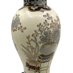 May include: A white porcelain vase with a gold bird finial and floral designs in shades of pink, gray, and black. The vase has a black base and is sitting on a black velvet stand.