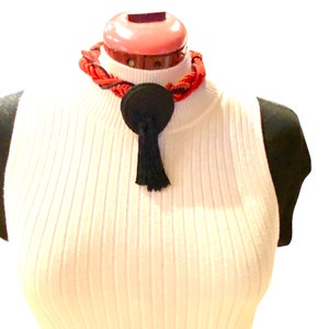 May include: A black and red rope necklace with a black tassel. The necklace is on a white mannequin.