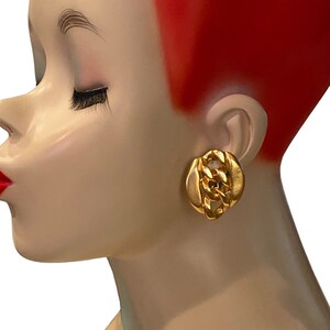 Puede incluir: Pendientes de cadena de eslabones de color dorado con un diseño grueso. Los pendientes se muestran en la oreja de un maniquí.