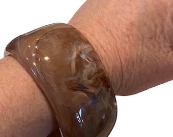 May include: A brown and white marbled resin bangle bracelet. The bracelet is thick and has a rounded shape.
