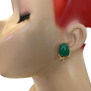 Op de afbeelding: Een paar gouden oorbellen met groene ovale cabochons. De oorbellen hebben een bloemmotief.