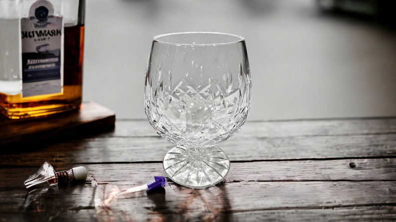 May include: A clear crystal glass with a cut design sits on a wooden surface. The glass is empty and has a round base.