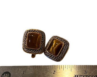 Könnte beinhalten: Ein Paar Ohrringe in Gold- und Silbertönen mit braunen Tigeraugen-Steinen. Die Ohrringe sind quadratisch und haben einen seilartigen Rand.