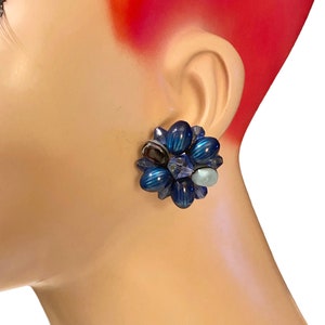 May include: A pair of blue and iridescent flower-shaped clip-on earrings. The earrings are made of glass beads and have a silver tone metal backing.
