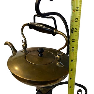 Può includere: Una teiera in ottone con manico e coperchio neri si trova su un supporto in ferro battuto con un design decorativo a volute. Il supporto è alto 40,6 cm.