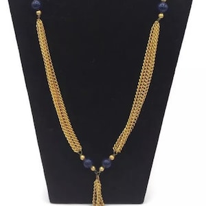 Puede incluir: Un collar de cadena dorada con un borla de cuentas azules. El collar está hecho de múltiples hebras de cadena y tiene cuentas azules en la parte superior e inferior.