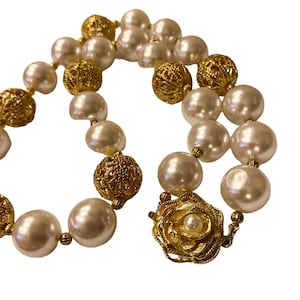 Könnte beinhalten: Eine weiße Perlen- und Goldkette mit einem dekorativen Verschluss. Die Kette besteht aus abwechselnd großen weißen Perlen und goldenen Filigran-Kugeln.