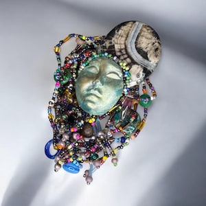 May include: A colorful beaded necklace with a green face mask and a brown and white agate stone pendant.