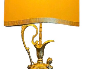 May include: A gold-toned table lamp with a decorative pitcher-shaped base and a yellow lampshade with a gold trim. The lamp base features intricate floral and scrollwork details.