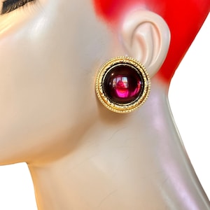 May include: A pair of gold-tone clip-on earrings with a large, round, purple cabochon stone.