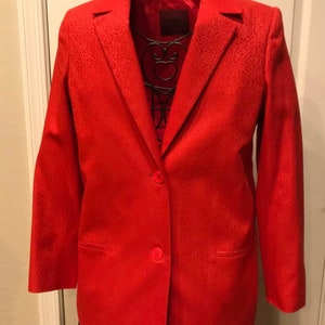 May include: A red blazer with a subtle patterned design. The blazer has a single button closure and two pockets.