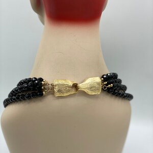 Pu&ograve; includere: Una collana multifilo di perle nere con una chiusura dorata. La collana &egrave; su un manichino.