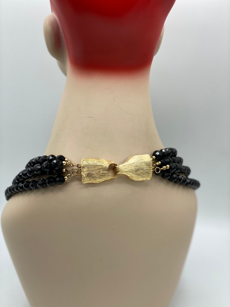 Pu&ograve; includere: Una collana multifilo di perle nere con una chiusura dorata. La collana &egrave; su un manichino.