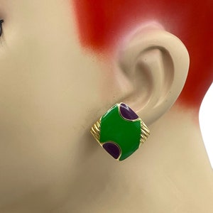 May include: A pair of green and purple enamel earrings with a gold-tone finish. The earrings are square-shaped with rounded corners and feature a geometric design.