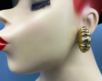 May include: A pair of gold-toned hoop earrings with a textured, ribbed design. The earrings are shown on a mannequin's ear.