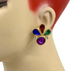 Könnte beinhalten: Ohrclips in Goldton mit einem Design aus violetten, roten, blauen und grünen Steinen. Die Steine sind in einem goldfarbenen Metallrahmen gefasst.