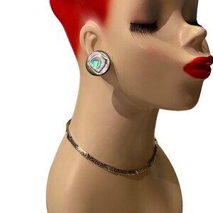 May include: A pair of round iridescent abalone shell earrings with a silver backing. The earrings are on a mannequin with red hair.