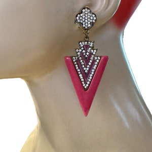 May include: Pink and gold tone statement earrings with a geometric design and clear crystal accents.