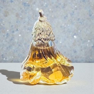 May include: A decorative glass flower-shaped object with a gold-colored top and a transparent, amber-colored body. The object has a textured surface and is likely a decorative piece or a bottle stopper.