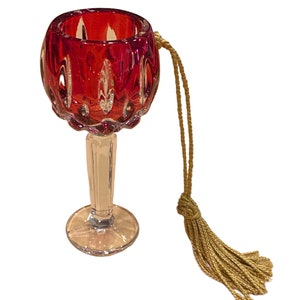 May include: A small, red glass goblet with a clear stem and base. It has a gold tassel attached to the top.