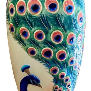 May include: A ceramic vase with a peacock design. The vase is white with a blue, green, and pink peacock with its tail feathers spread out. The peacock's eyes are blue and pink.
