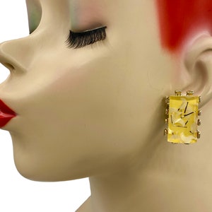 May include: A pair of gold tone clip-on earrings with a yellow rectangular stone. The stone has a white marbled pattern.