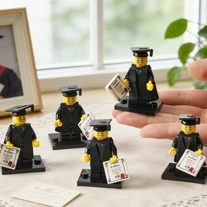 May include: A collection of Lego graduation figurines, each wearing a black cap and gown, holding a diploma. The figurines are on black bases. A framed graduation photo is in the background.