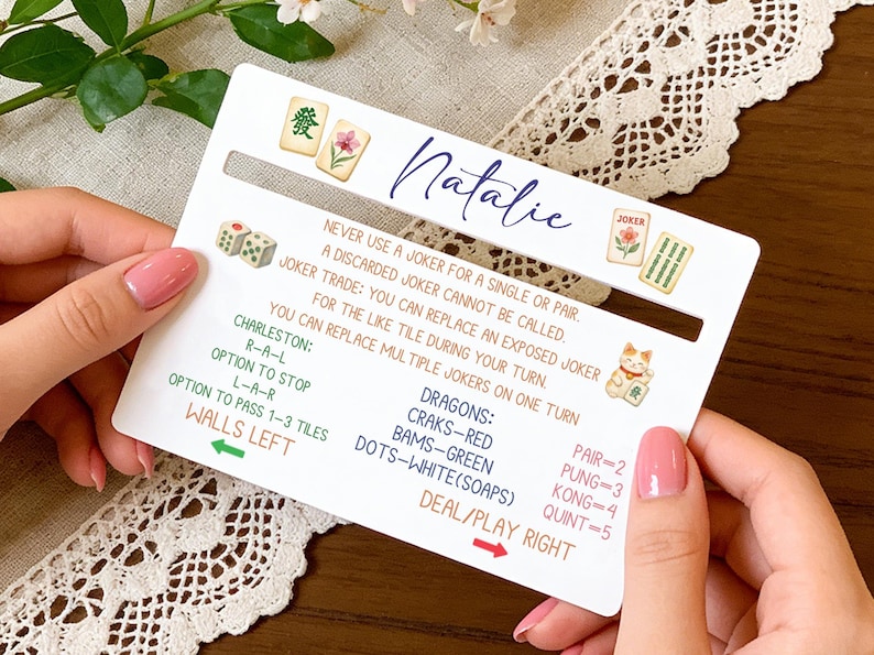 May include: A white card with Mahjong game rules and the name "Natalie" in cursive. The card features illustrations of dice, tiles, and a lucky cat. Text includes game instructions and scoring details.