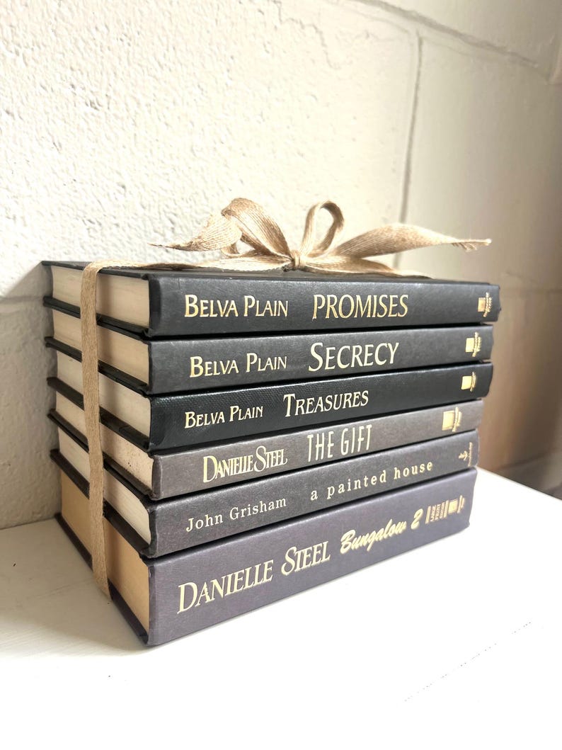 May include: A stack of eight black and gray hardcover books with gold lettering. The titles are "Promises", "Secrecy", "Treasures", "The Gift", "a painted house", and "Bungalow 2". The authors are Belva Plain and Danielle Steel.