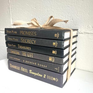 May include: A stack of eight black hardcover books with gold lettering on the spines. The books are tied together with a brown ribbon. The titles of the books are "Promises", "Secrecy", "Treasures", "The Gift", "A Painted House", and "Bungalow 2".