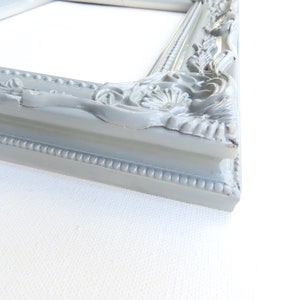 May include: A grey ornate picture frame with a decorative, raised design. The frame is made of wood and has a smooth finish.
