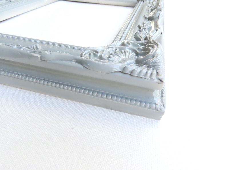 May include: A grey ornate picture frame with a decorative, raised design. The frame is made of wood and has a smooth finish.