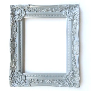 May include: A silver ornate picture frame with a decorative, detailed design. The frame is made of wood and has a smooth, matte finish.