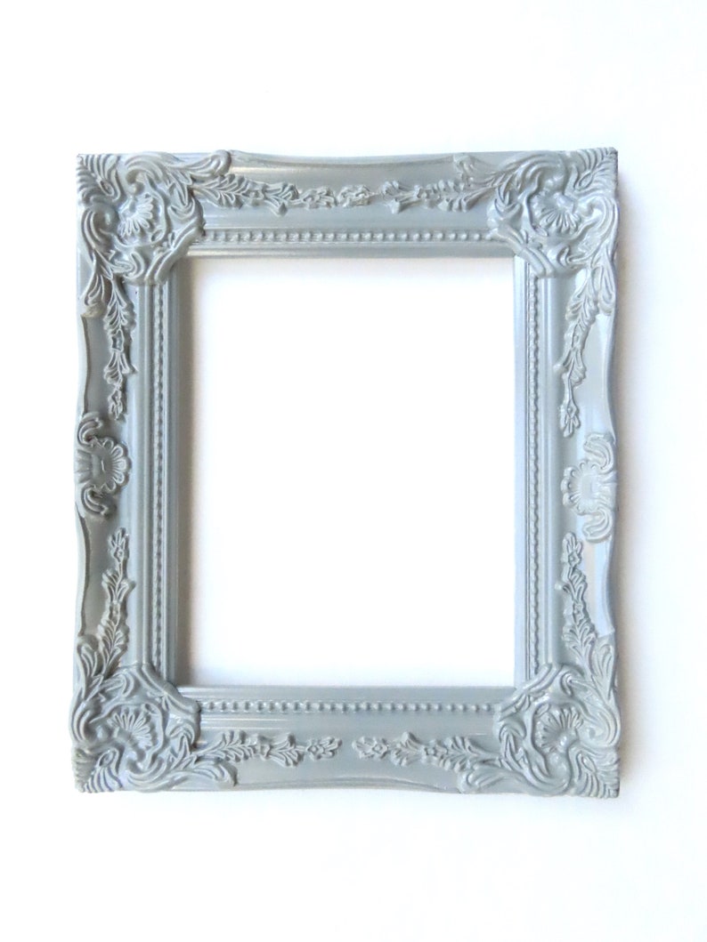 May include: A silver ornate picture frame with a decorative, detailed design. The frame is made of wood and has a smooth, matte finish.
