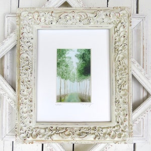 May include: A framed watercolor painting of a forest scene. The artwork features a path leading into a grove of green trees. The painting is set within a white mat and an ornate, off-white, distressed wooden frame.