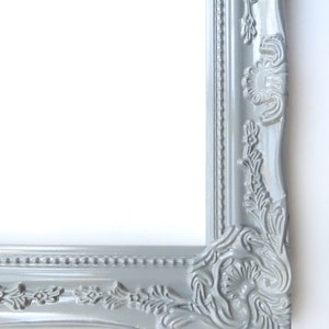May include: A grey ornate picture frame with a decorative, detailed design. The frame is made of wood and has a smooth, painted finish.