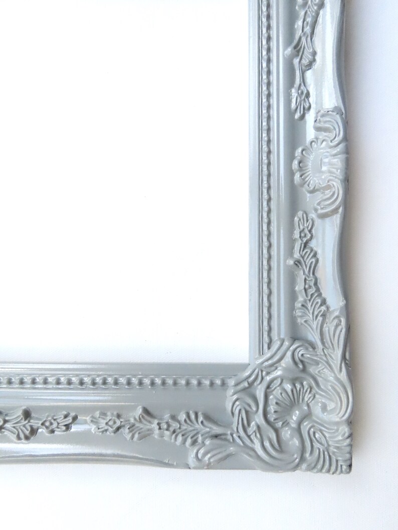 May include: A grey ornate picture frame with a decorative, detailed design. The frame is made of wood and has a smooth, painted finish.