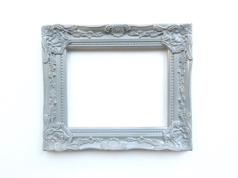 May include: A grey ornate picture frame with a white background. The frame has a decorative design with floral motifs.