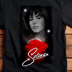 Op de afbeelding: Witte en zwarte T-shirts met een portret van Selena met een rode roos en de naam "Selena" in cursief. De afbeelding is een zwart-wit portret met een rode roos.