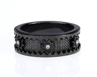 May include: Black ring with a textured surface and three small clear gemstones. The ring has a gear-like design.